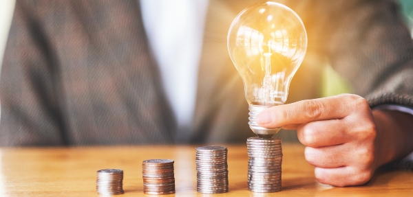 Close-up shot of businesswoman holding and putting lightbulb on coins stack on a table.