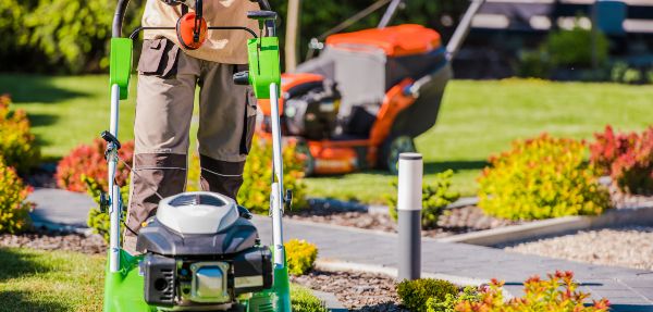 Male Landscaper Doing Garden Maintenance Work with His Professional Equipment Using Two Different Lawn Mowers.