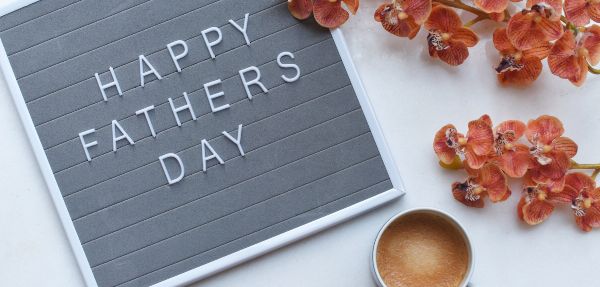 "Happy Fathers Day" written on a board, beside flowers and a cup of coffee.