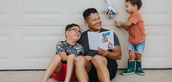 A father and his sons sharing smiles and laughter as he reads a Father's Day card.