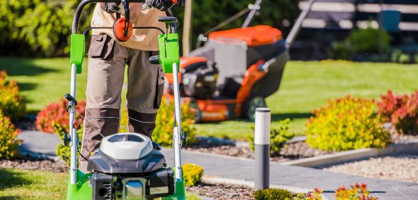 Male Landscaper Doing Garden Maintenance Work with His Professional Equipment Using Two Different Lawn Mowers.