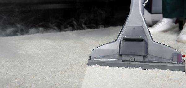 Close-up view of person cleaning white carpet with professional vacuum cleaner