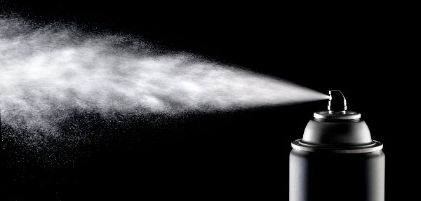 An aerosol can of spray dispensing its content against a backlit black background.