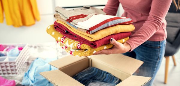 Woman folding her clothes and packing them in a delivery box.