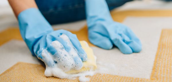 Partial view of woman in rubber gloves cleaning striped carpet with foamy sponge