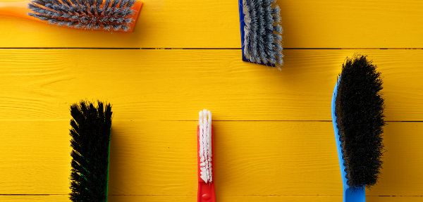 Household cleaning brushes on a yellow wooden background.