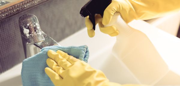 Cropped image of person using a cloth and a detergent while cleaning sink and tap in bathroom.