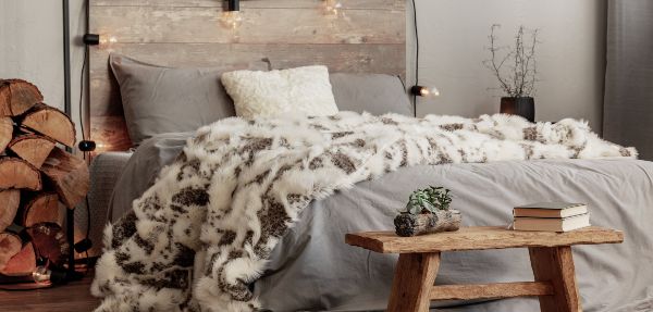 Wooden bench at the foot of the bed with grey bedding and a cosy blanket.