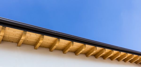 Low angle view of new house with wooden roof and gutter against clear blue sky.