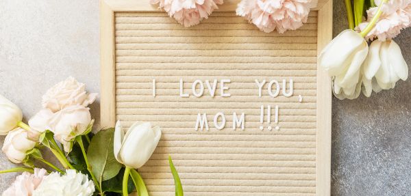 "I LOVE MOM" on a letterboard and beautiful spring flowers on a light background. View from above.