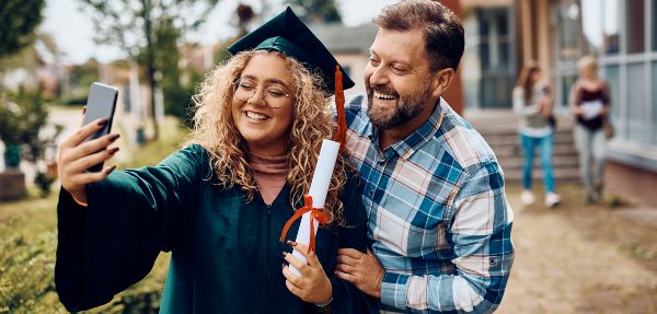 Happy university graduate and her father having fun while taking selfies with a smart phone.