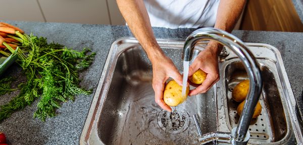 Man in kitchen washing vegetables.