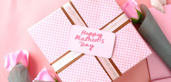 A Mother's Day gift wrapped in pink, with roses on either side of it.