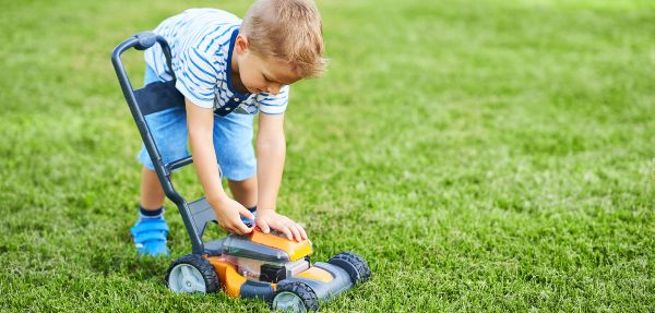 Picture of happy 3 year old boy having fun mowing lawn.