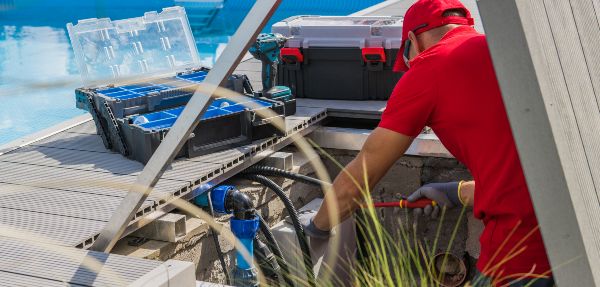 Closeup of Professional Worker in Red Uniform Fixing Outdoor Swimming Pool Heating System Using Different Tools. 