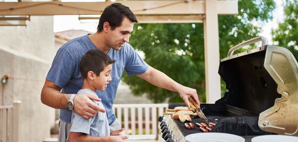 Father teaching son how to grill hot dogs while bonding.