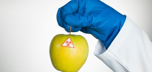 Toxic sticker on an apple being held up by a hand wearing a glove