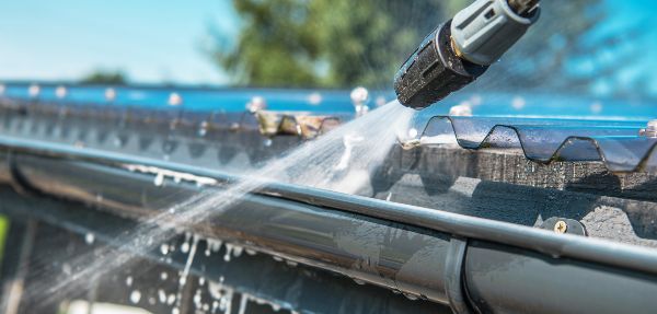 Cleaning a roof gutter using a pressure washer.