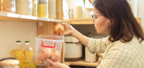 Woman in pantry organising onions and other foods.