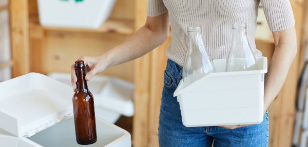 Close-up of a woman throwing out a glass bottle into a recycling bin.