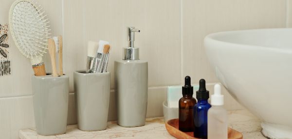 Set of serums, cups with brushes and liquid soap dispenser next to bathroom sink.