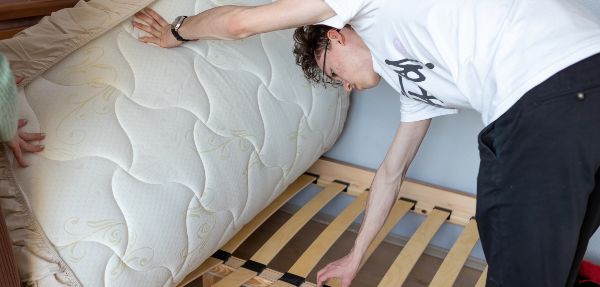 Man fixing a board beneath his mattress before flipping it.