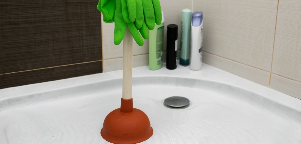 Plunger on a shower floor with gloves on top of it