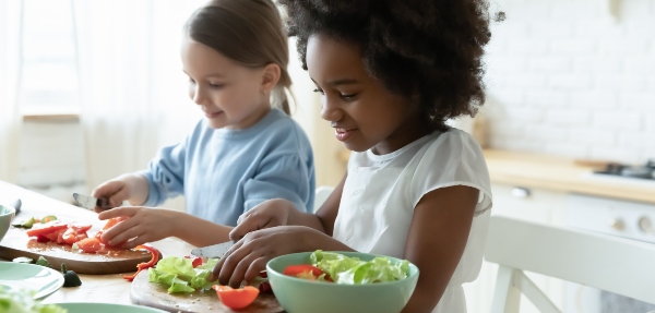 Two girls cutting vegetables on cutting boards to make a salad