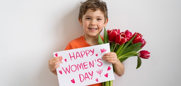 Little boy holding flowers and a card that says: "Happy Women's Day"