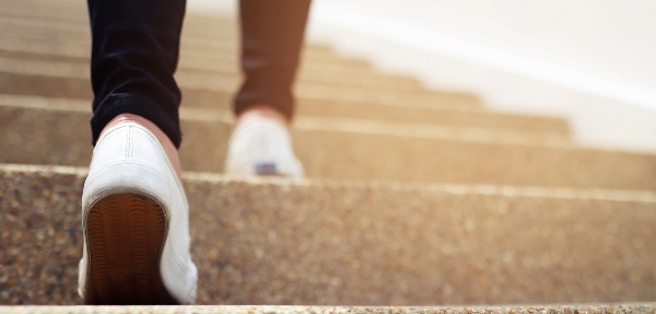 Close-up shot of a person walking up stairs, wearing black pants and white sneakers