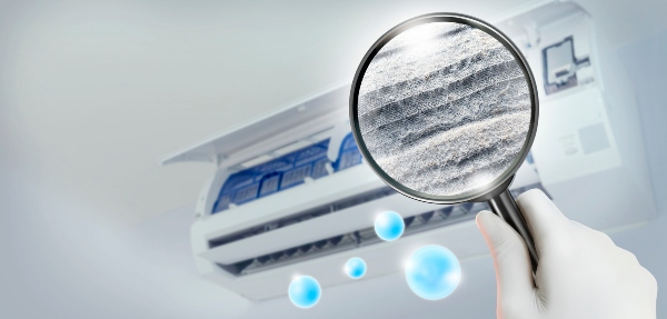 Hand holding up magnifying glass showcasing particles coming from an air conditioner