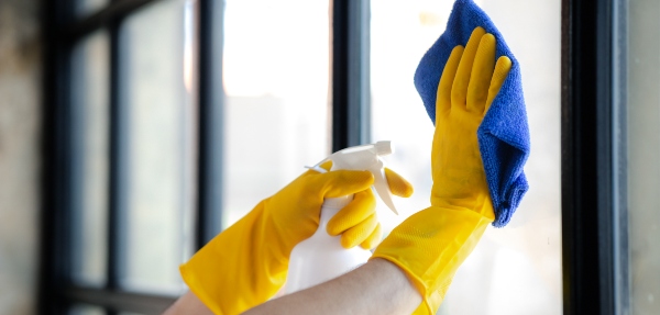 Close-up shot of a person with yellow gloves cleaning a window