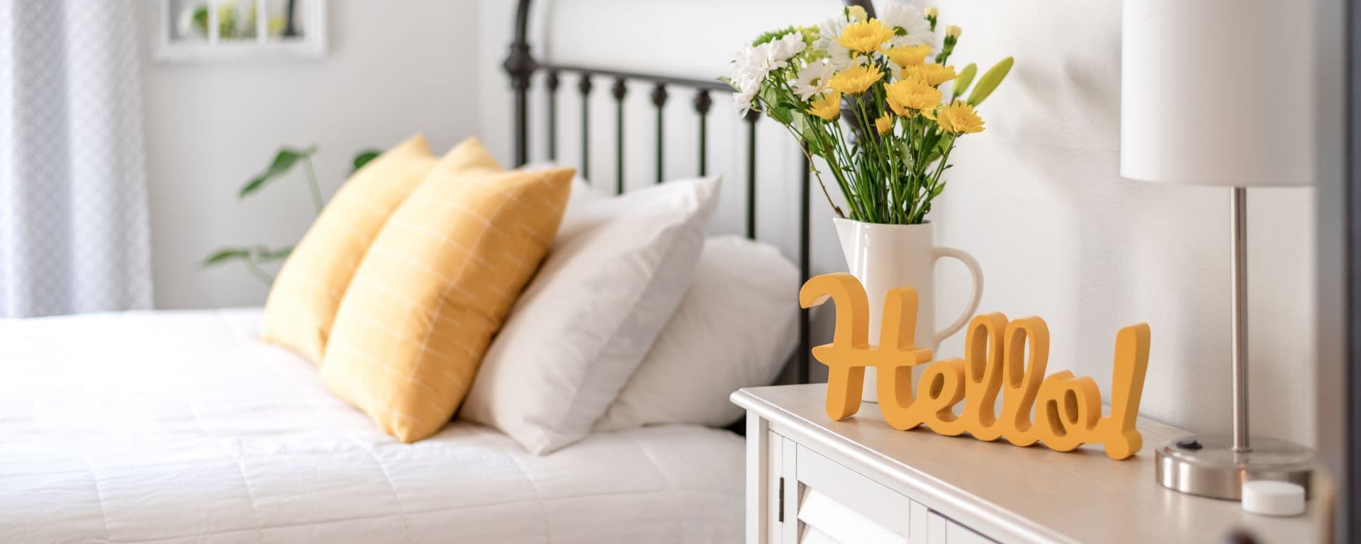 Cheerful yellow hello sign and fresh flowers in a clean and bright bedroom.