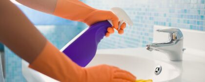 Person doing chores in bathroom at home, cleaning sink and tap with spray detergent.