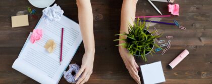 Top view of woman sorting out mess on working table, moving stationery, documents, food and plant.