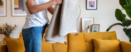 Person folding a blanket tying up the living room and cleaning the house.