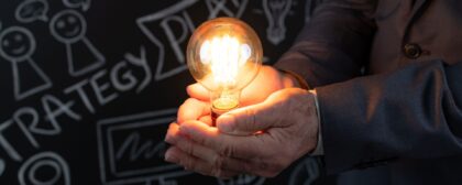 Businessman holding lightbulb in hand against blackboard