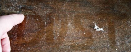 The word 'DUST' written out on a dusty table in between a large amount of dust.