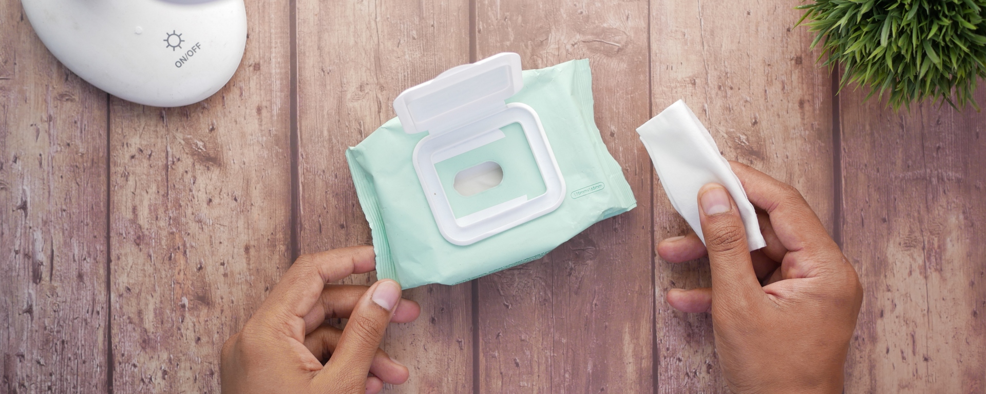 Person holding a wet wipe next to a pack of wet wipes on a wooden table