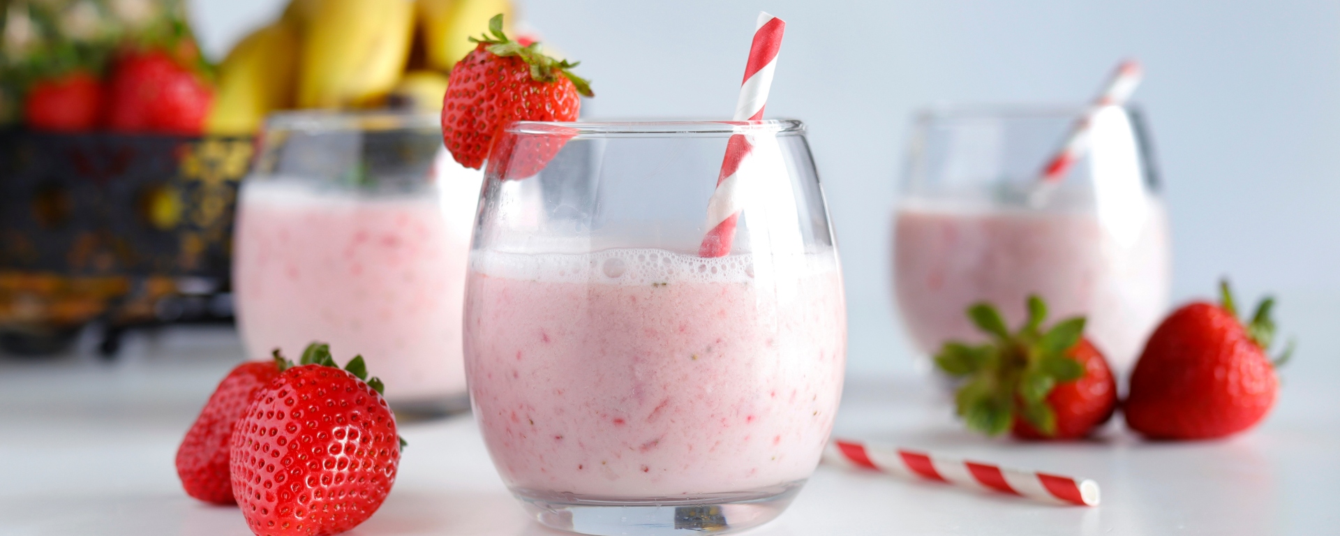 3 smoothies with straws and strawberries around them