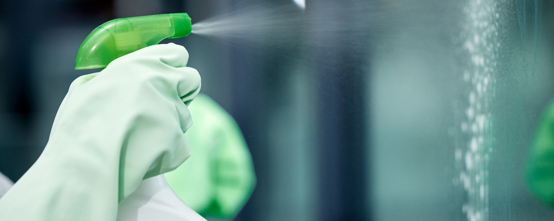 Close-up of a person's hand wearing a glove spraying a cleaning product onto a window