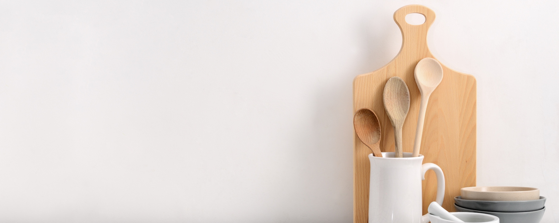 Cutting board behind wooden kitchen spoons in a mug