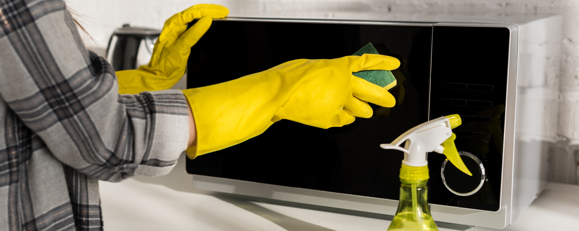 Cropped view of woman in rubber gloves cleaning a microwave with a sponge