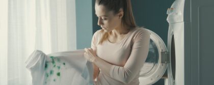 Disappointed woman standing next to the washing machine and holding stained clothes