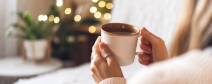 Woman's hand holding a mug in the foreground with living room decorations in the background